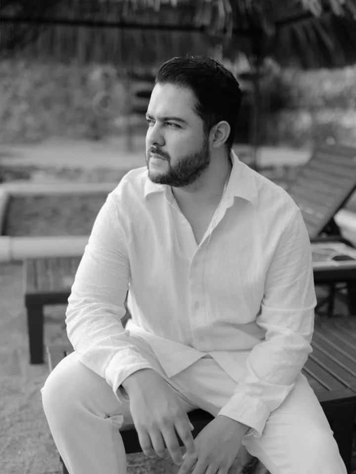 Josh Alvarado in a white linen shirt, seated outdoors and looking to the side